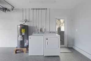 A laundry area with two washers and a dryer, a water heater, and a door leading to a balcony. - Beachside Oasis 🌴 Canal Front 4BR Home | Private Pool + Spillover Spa (Fort Myers Beach)