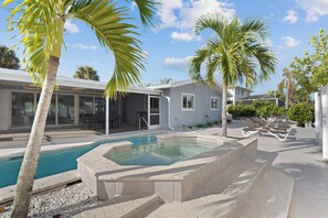 Una piscina con hidromasaje, rodeada de palmeras y un área de patio techada.