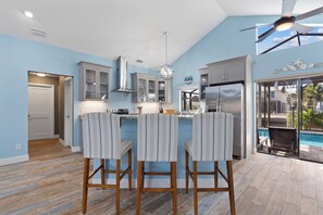 A kitchen with a central island, bar stools, a ceiling fan, and a view of a pool. - Canal Paradise Retreat 🌴⛵ Dock + Heated Pool | Near Times Square (Fort Myers Beach)