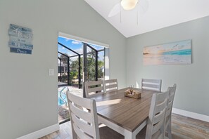 A dining area with a wooden table and chairs, a painting of a beach scene, and a sign on the wall. - Canal Paradise Retreat 🌴⛵ Dock + Heated Pool | Near Times Square (Fort Myers Beach)