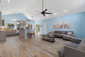 Un salon moderne avec un canapé d’angle, une table basse et un coin repas comprenant des chaises, et une cuisine en arrière-plan.