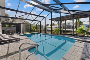 A swimming pool with a glass enclosure, lounge chairs, and a patio area. - Canal Paradise Retreat 🌴⛵ Dock + Heated Pool | Near Times Square (Fort Myers Beach)