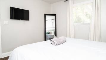 Ein Hotelzimmer mit einem Bett, einem flachbildfernseher an der Wand, einem Fenster mit Jalousien und einem Handtuch auf dem Bett.