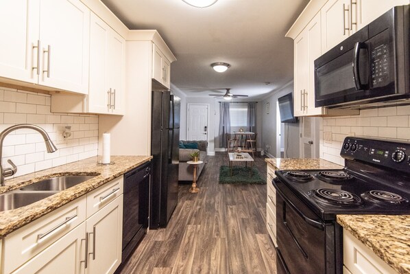 A kitchen with white cabinets, a black refrigerator, a microwave, and a stove. - Entire 2 BD Rental Unit near Dwtn Atlanta (East Point)