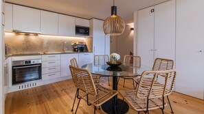A modern kitchen with white cabinetry, a built-in oven, and a dining area with wicker chairs and a glass table. - Design 2BR Duplex with AC by LovelyStay (Lisboa)