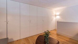 Une pièce avec un plancher en bois, une table ronde ornée d’une plante et une grande armoire blanche à portes.