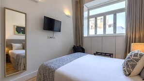 A hotel room with a bed, a television mounted on the wall, a window with curtains, and a mirror reflecting part of the room. - Design 2BR Duplex with AC by LovelyStay (Lisboa)