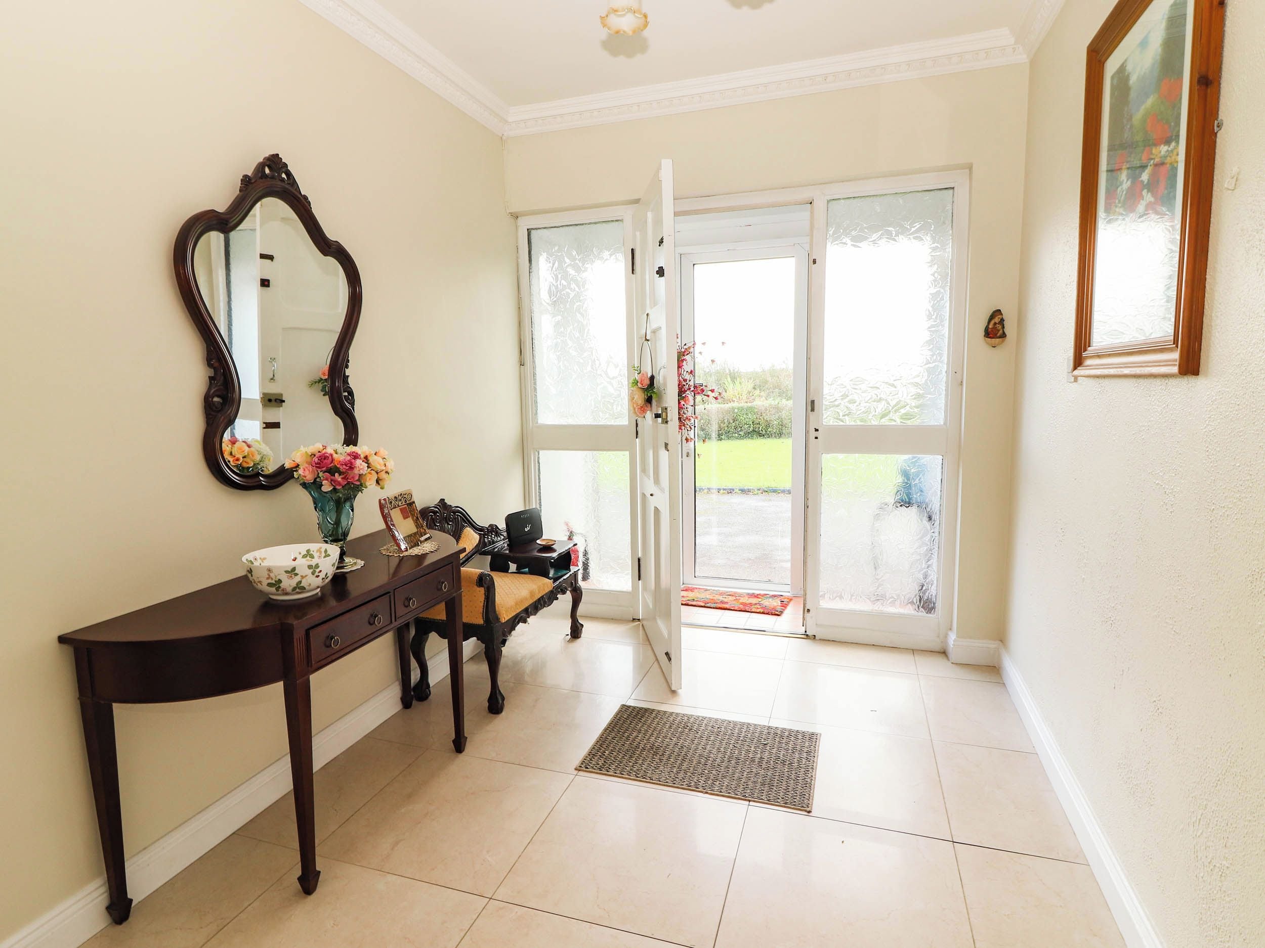 A room with a wooden console table, a mirror, a vase with flowers, and a bench.