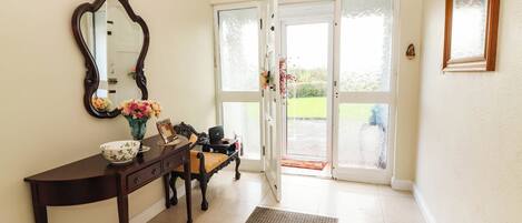 A room with a wooden console table, a mirror, a vase with flowers, and a bench.