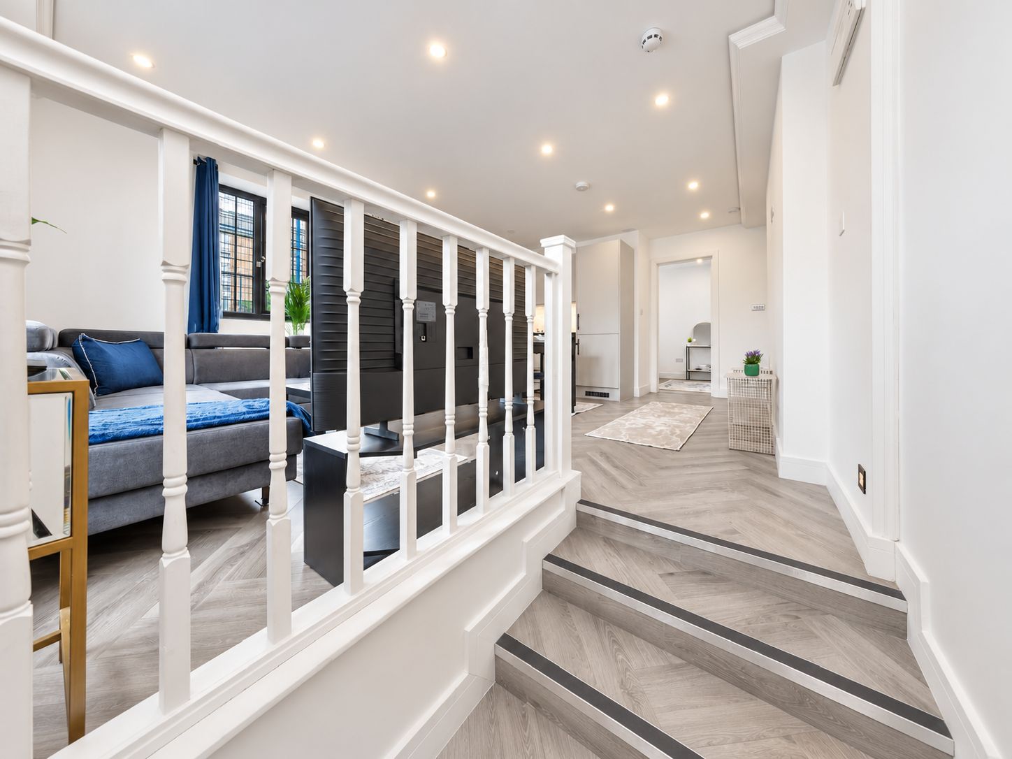 Un intérieur moderne avec un escalier, un espace de vie comprenant un canapé et un téléviseur, et une cuisine en arrière-plan.