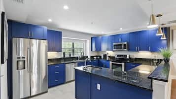 A modern kitchen with blue cabinets, stainless steel appliances, and a granite countertop.