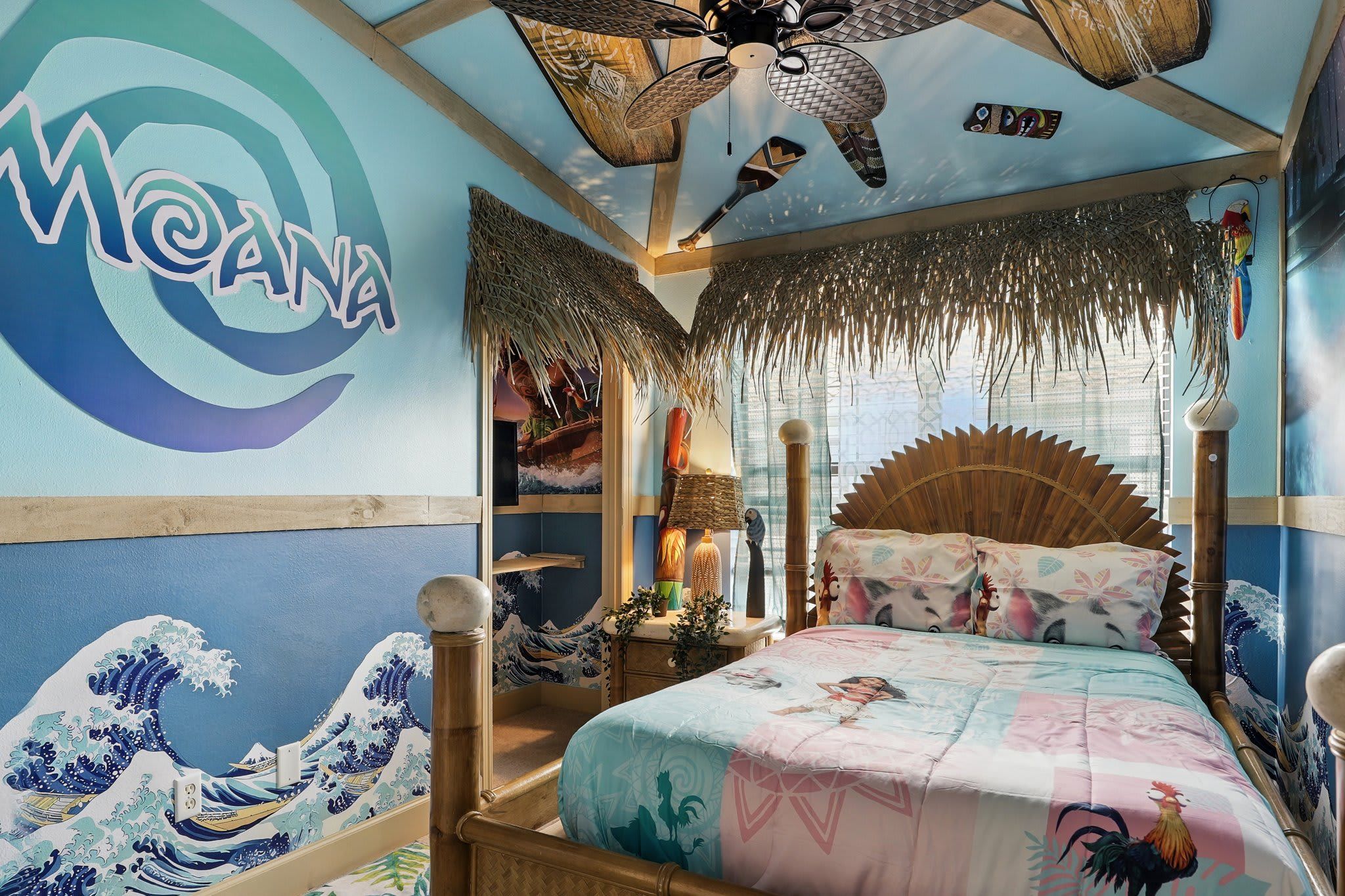 A room with a traditional Japanese wave painting, a bed with a colorful quilt, and a ceiling fan.