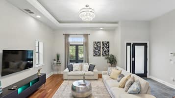 Uma sala de estar espaçosa com uma grande televisão de tela plana, um candelabro, um conjunto de sofás e uma mesa de centro.