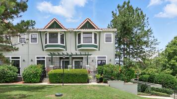 A two-story house with a green facade, a covered porch, and a well-maintained garden.