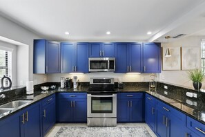 A modern kitchen with blue cabinets, stainless steel appliances, and a granite countertop.