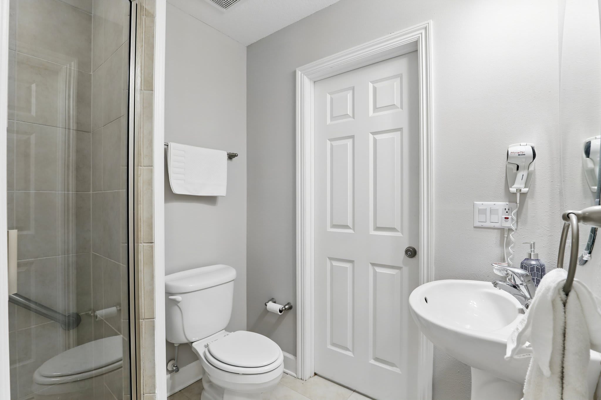 Un baño con cabina de ducha de vidrio, un inodoro blanco, un lavamanos blanco y una puerta blanca.