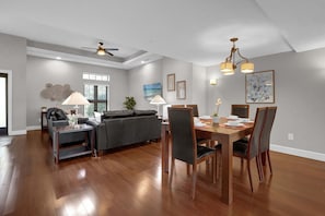Uma sala de estar ampla com um sofá, uma mesa de jantar posta para quatro e um ventilador de teto.