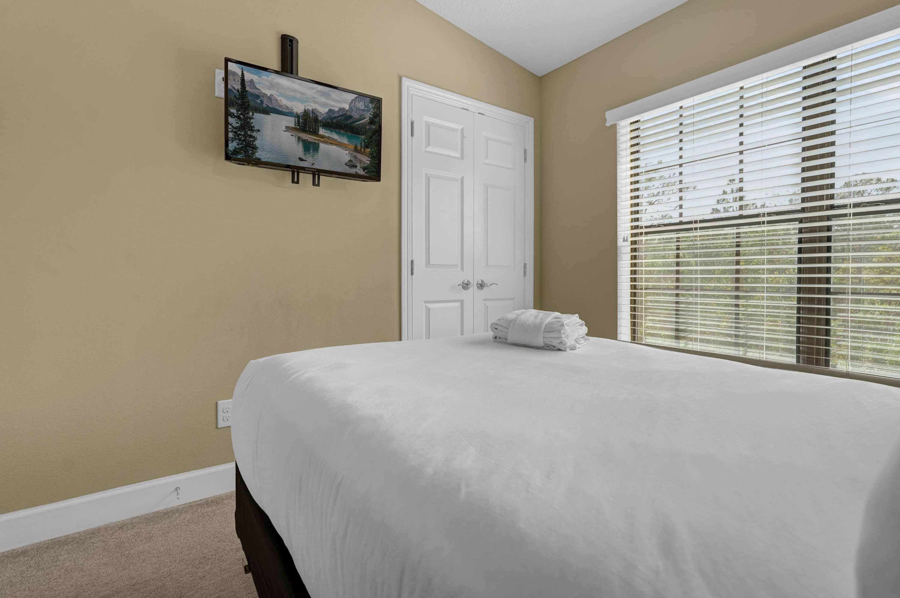 Un dormitorio con cama, una puerta, una ventana con persianas y un cuadro en la pared.