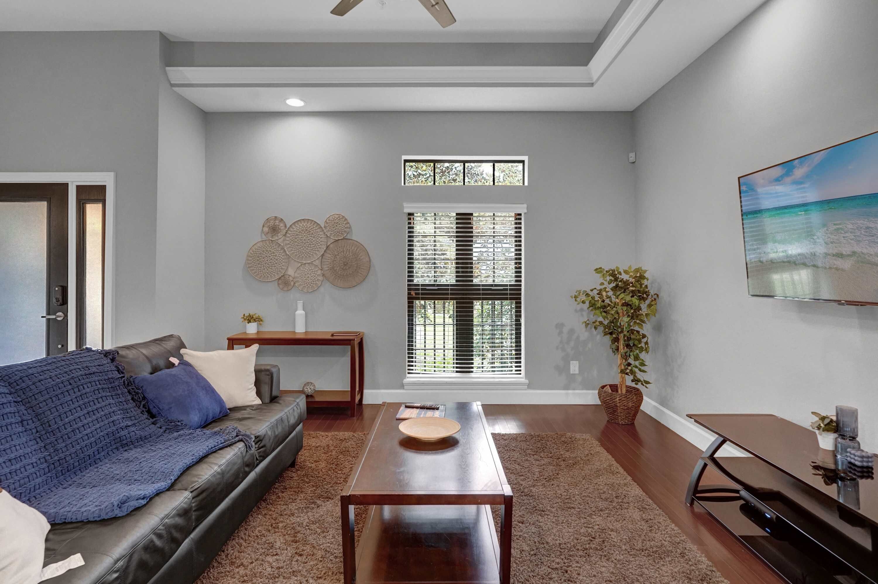 A modern living room with a leather sofa, a coffee table, a TV, and a large window with blinds.