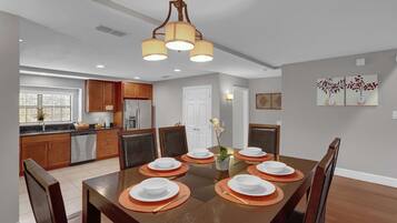 A dining area with a wooden table set for six, surrounded by chairs, in a modern kitchen with wooden cabinets and a built-in oven.