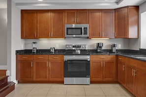 A modern kitchen with wooden cabinets, a built-in microwave, a stove, and a coffee maker. - 4 BD Townhome Close to Disney! (Orlando)
