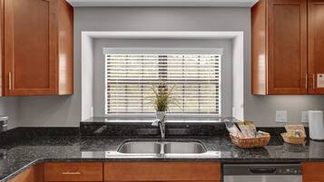A kitchen with wooden cabinets, a granite countertop, a stainless steel sink, and a window with blinds.