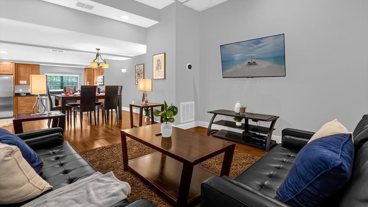 Una sala de estar moderna con comedor, un televisor de pantalla plana montado en la pared y una cocina al fondo.