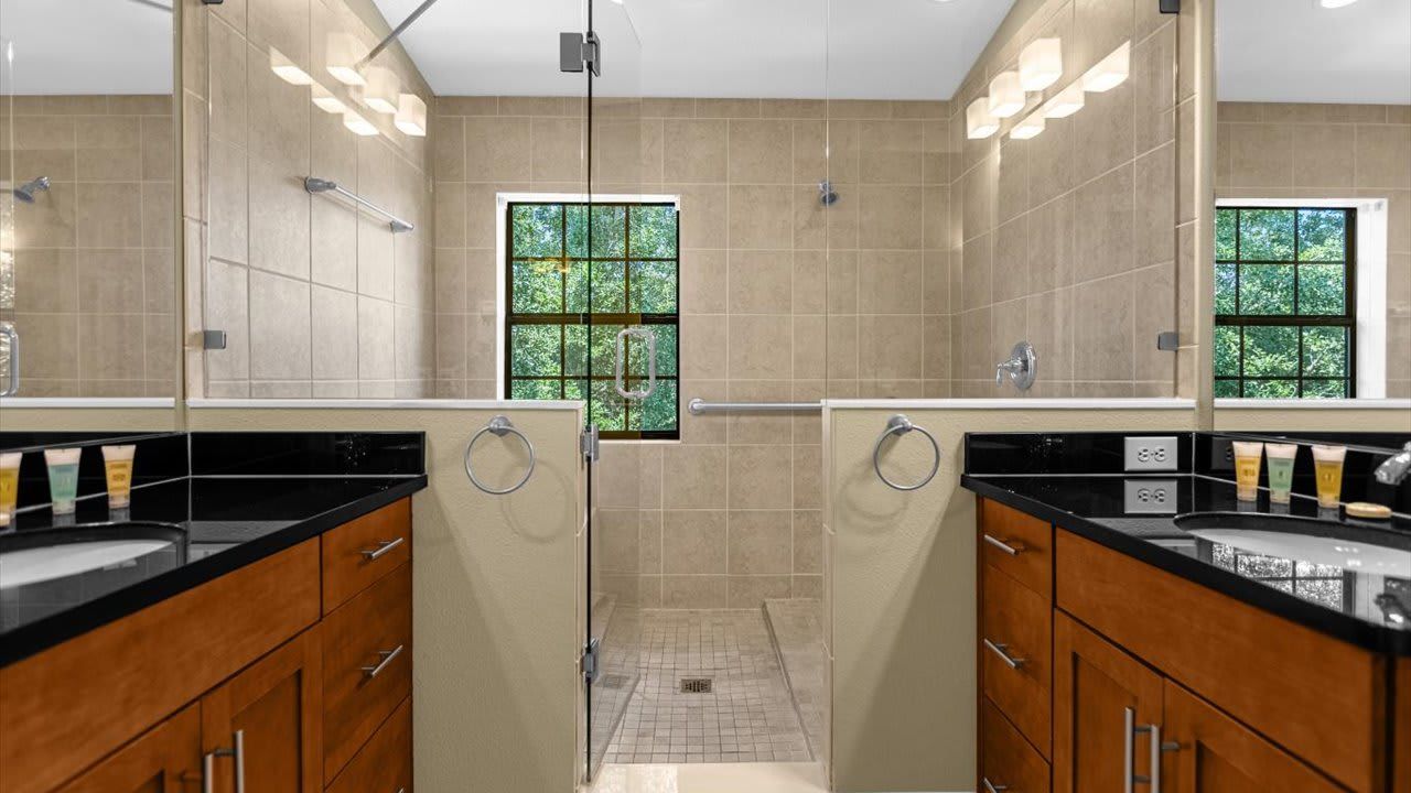 A modern bathroom with dual sinks, a shower area, and a window providing natural light.