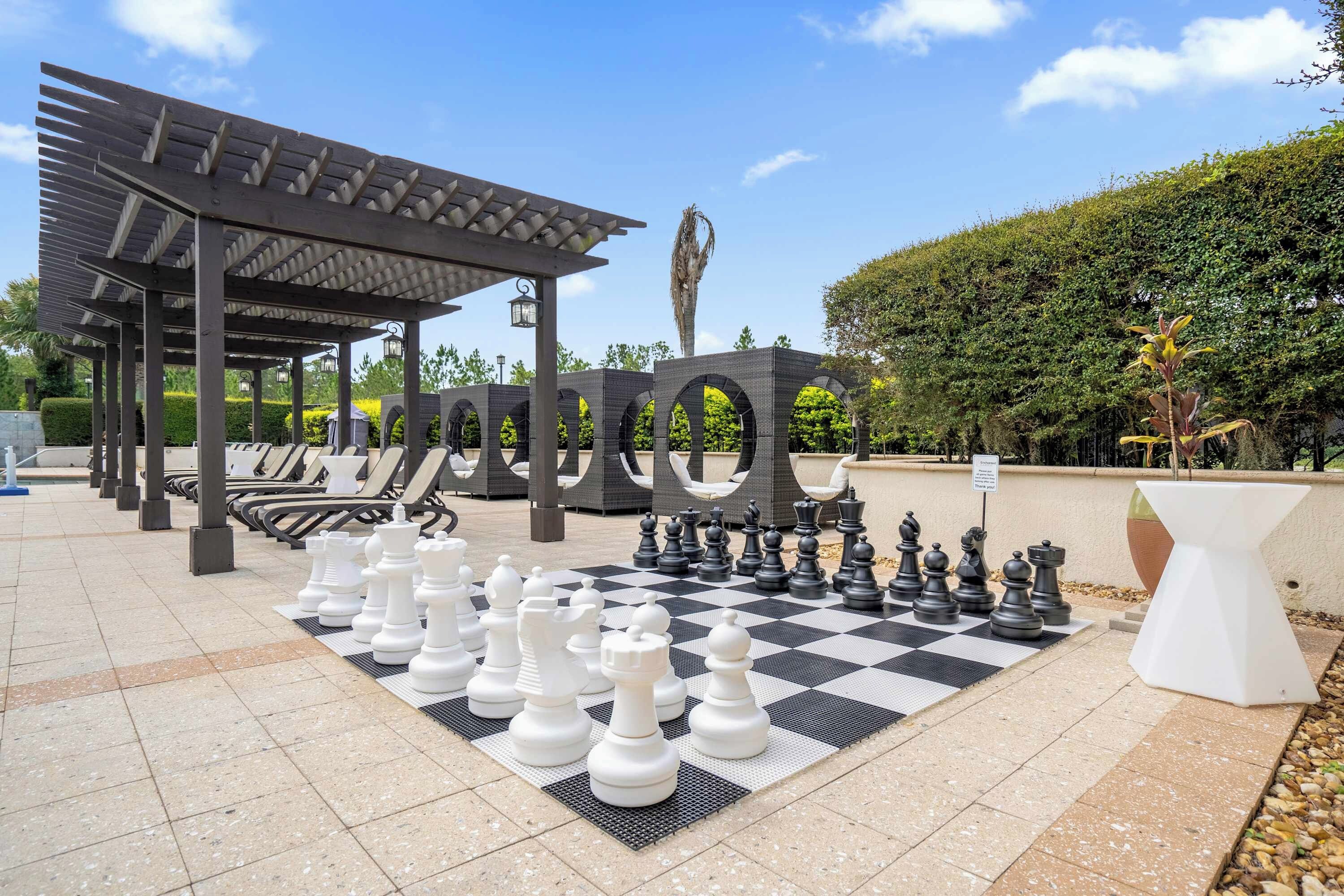 A chessboard set up outdoors with a pergola and lounge chairs in the background.