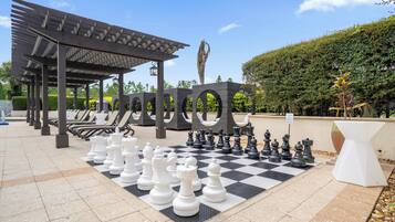 A chessboard set up outdoors with a pergola and lounge chairs in the background.