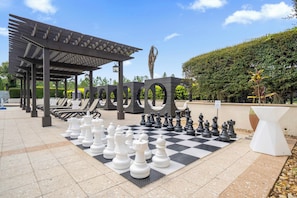 A chessboard set up outdoors with a pergola and lounge chairs in the background. - Family Disney Getaway With Pool, Spa and Billiards (Orlando)