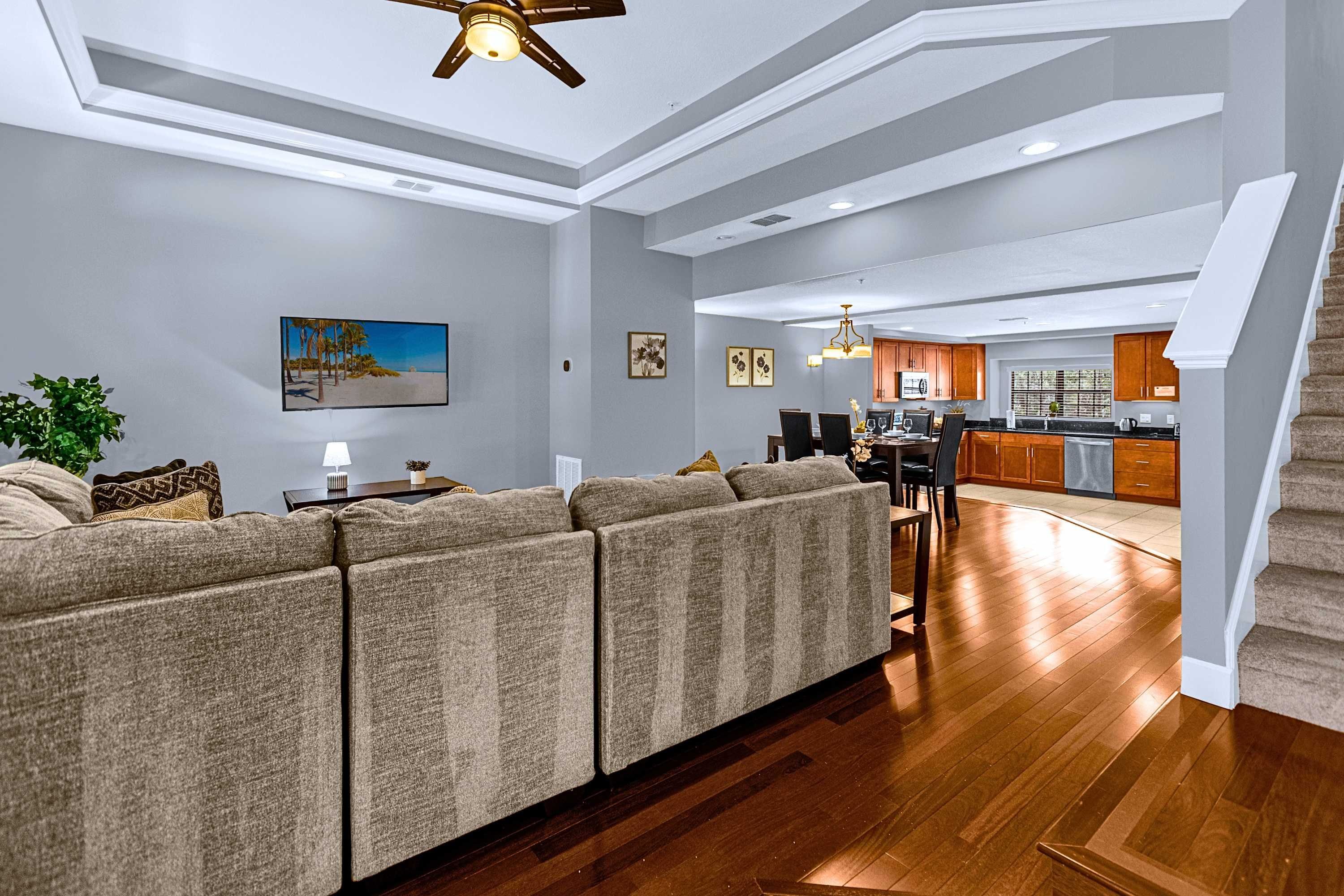 Uma sala de estar moderna com sofá seccional, área de jantar e cozinha com armários de madeira.