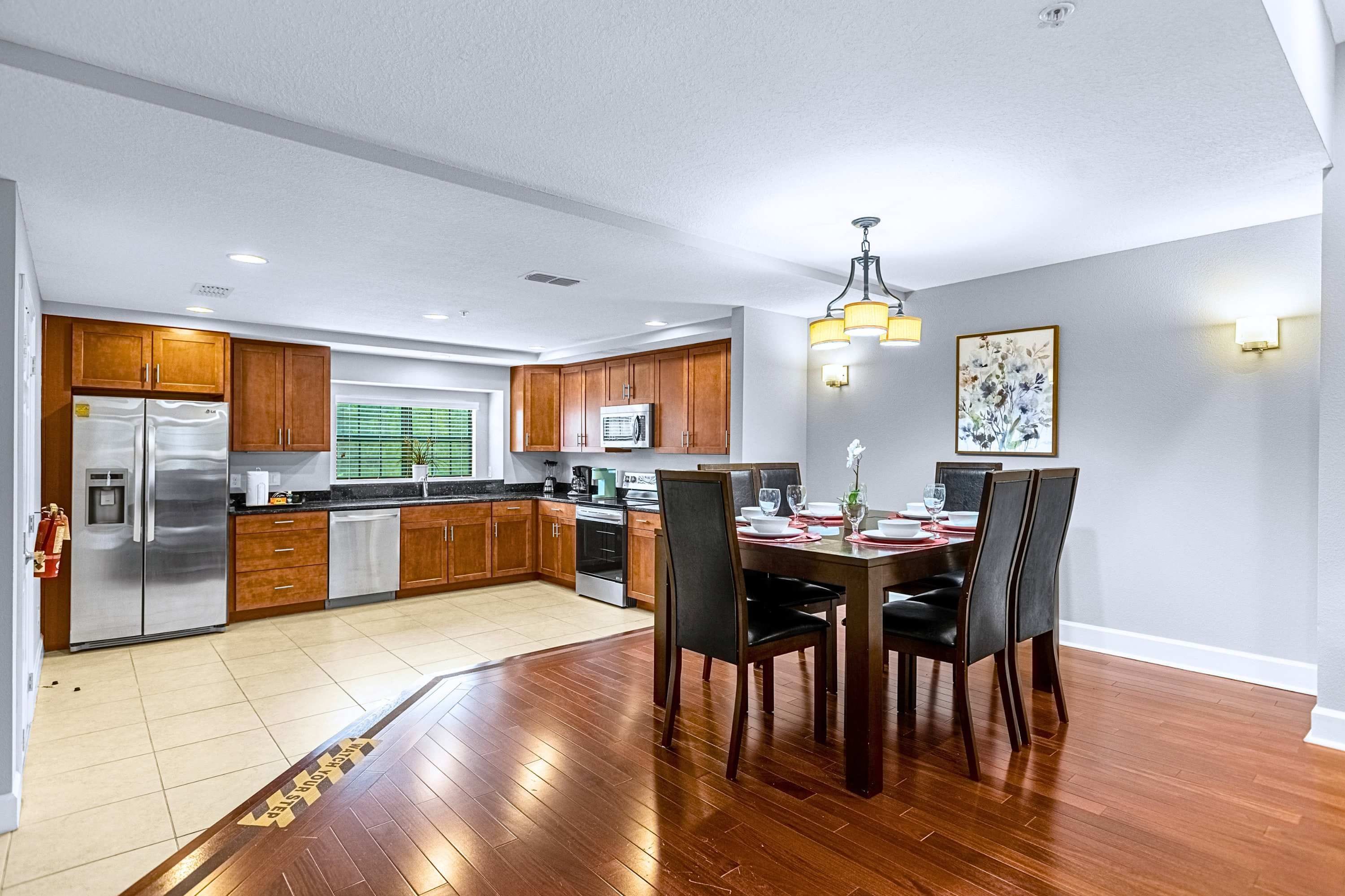 Una cocina moderna con electrodomésticos de acero inoxidable, armarios de madera y un comedor con una mesa dispuesta para cuatro.