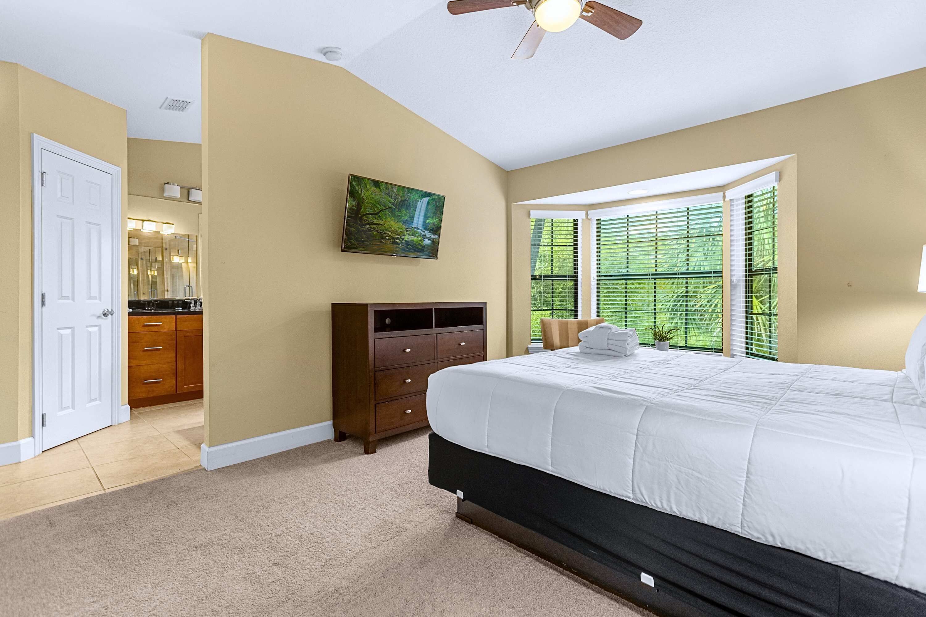 A bedroom with a large bed, a dresser, a painting, and a window with blinds.