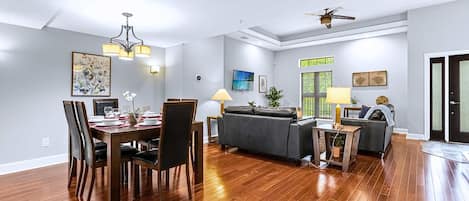A spacious living area with a dining table, sofas, and a ceiling fan.