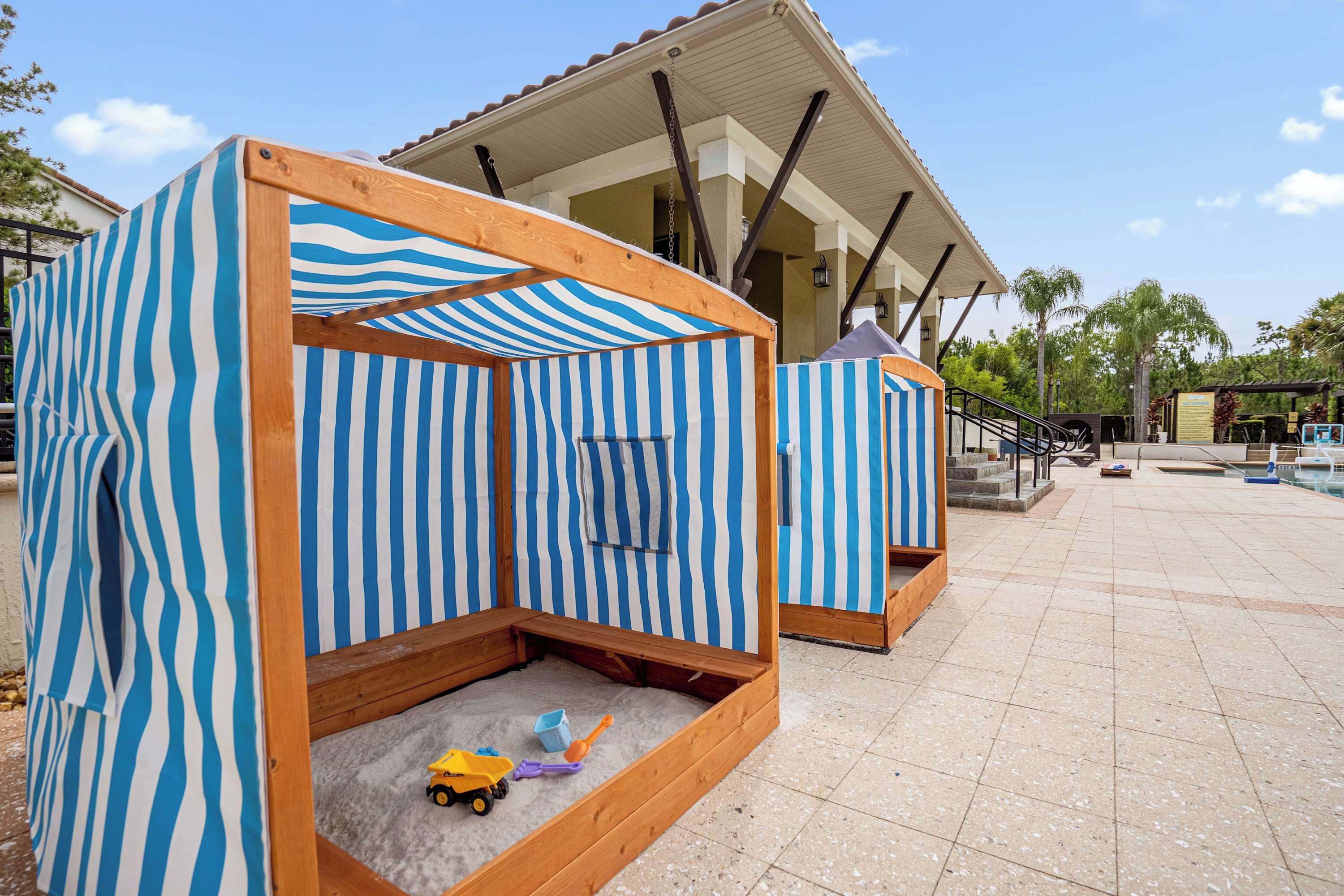 Espaço de brincadeiras com tema praiano, com tendas listradas e chão de areia.