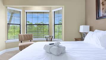 Quarto de hotel com cama grande, uma cadeira, mesa pequena e janela com persianas.