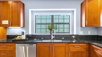 A kitchen with wooden cabinets, a black countertop, a stainless steel sink, and a window with blinds.