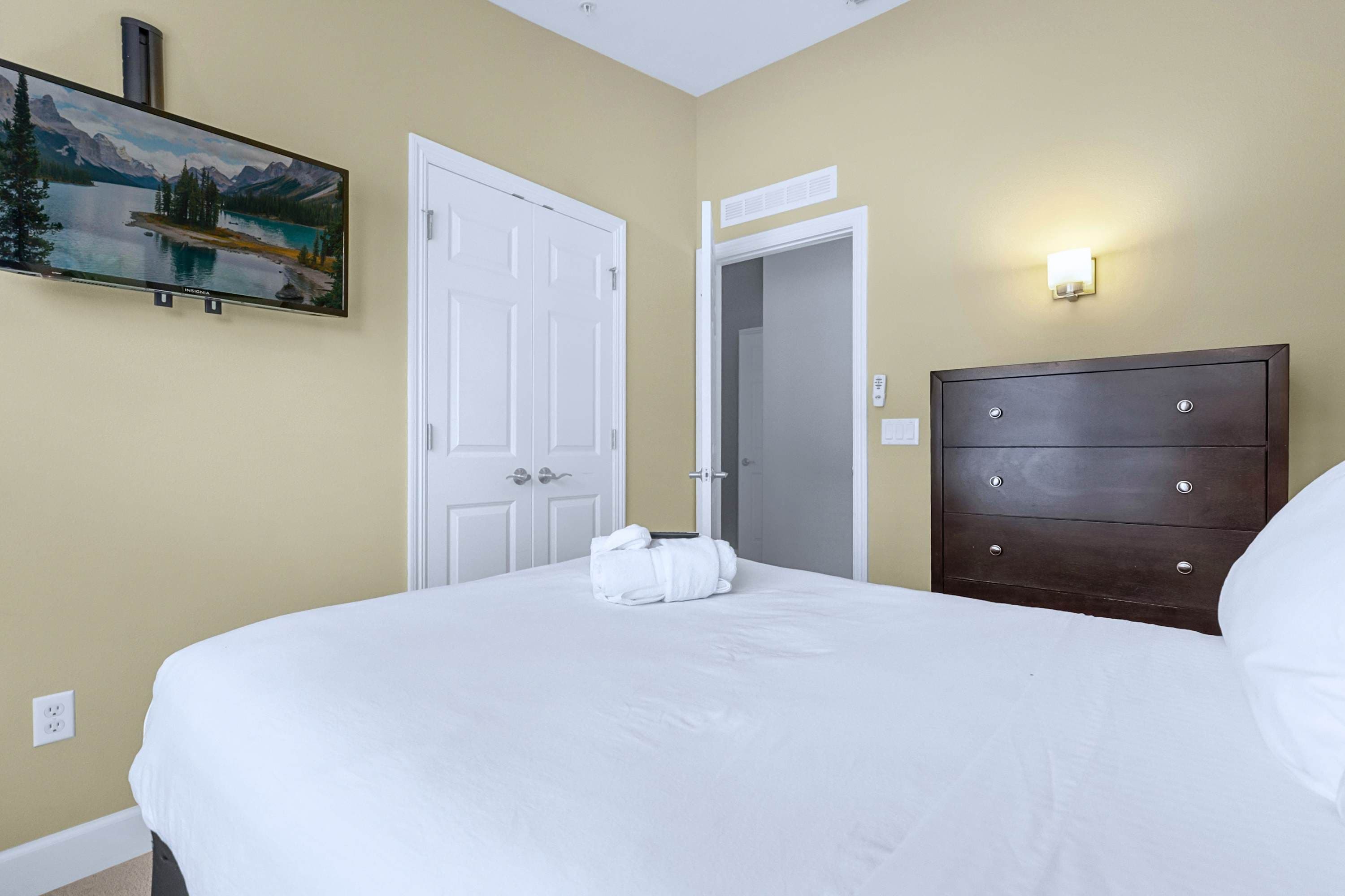 Una habitación de hotel con una cama, un aparador, un cuadro y una puerta que da a un baño.