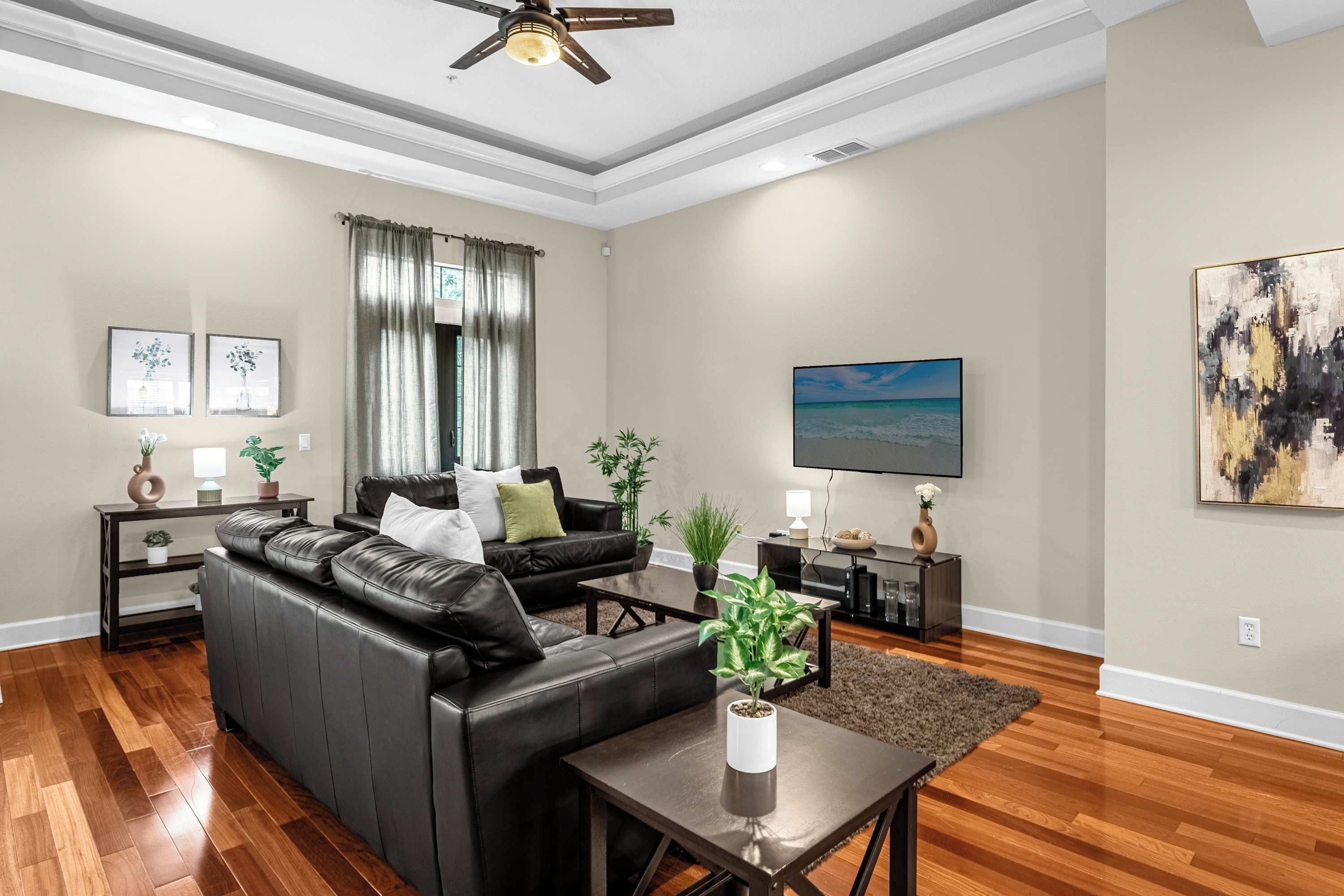 A living room with a black leather sofa, a coffee table, a ceiling fan, and a painting on the wall.