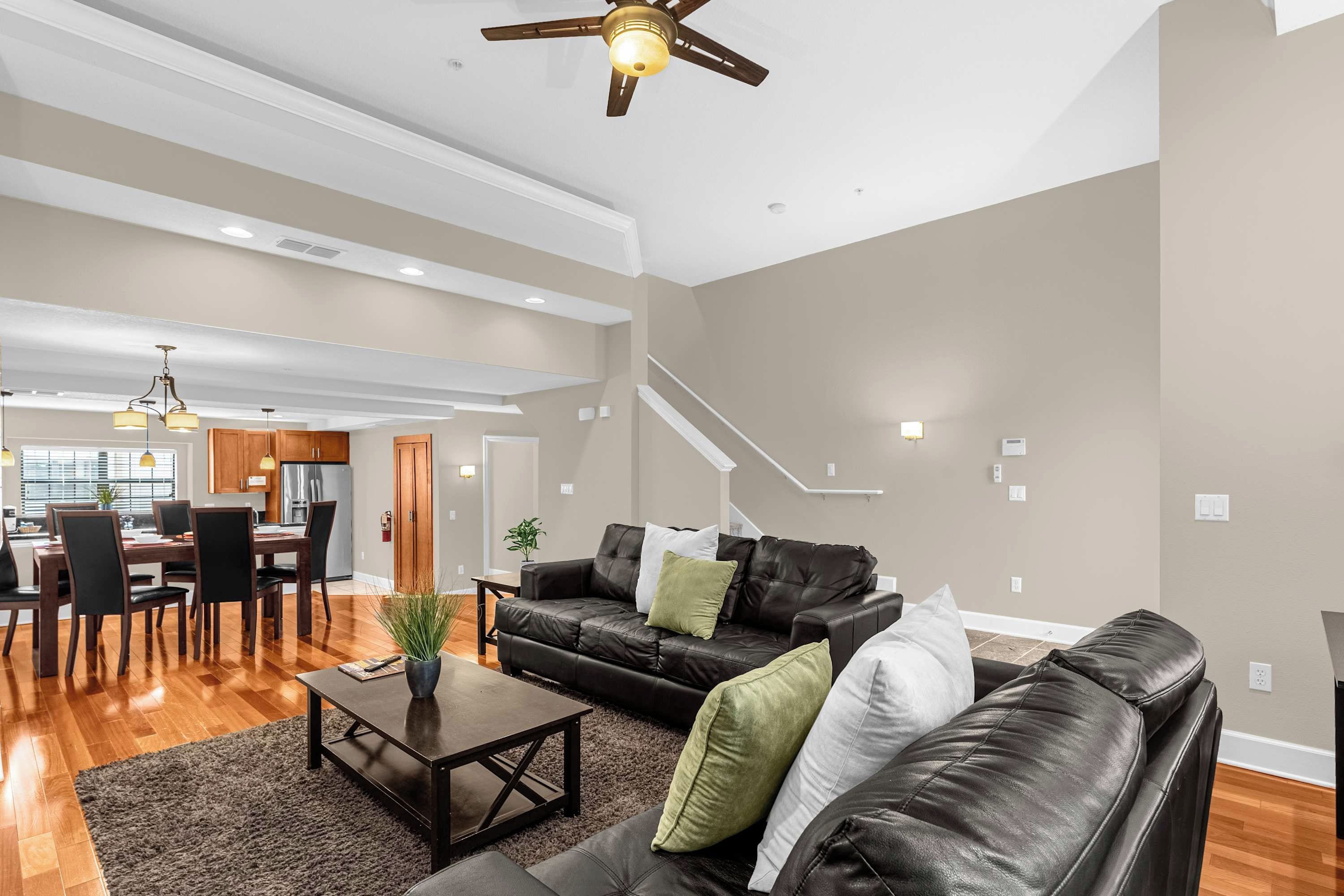 A spacious living room with a black leather sofa, a coffee table, and a dining area with wooden furniture.