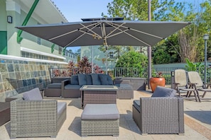 Un espace extérieur aménagé avec des meubles en osier, un grand parasol et une plante en pot.