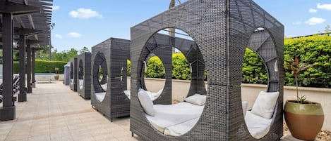 Outdoor wicker seating areas with cushions, a pergola structure, and a large planter.