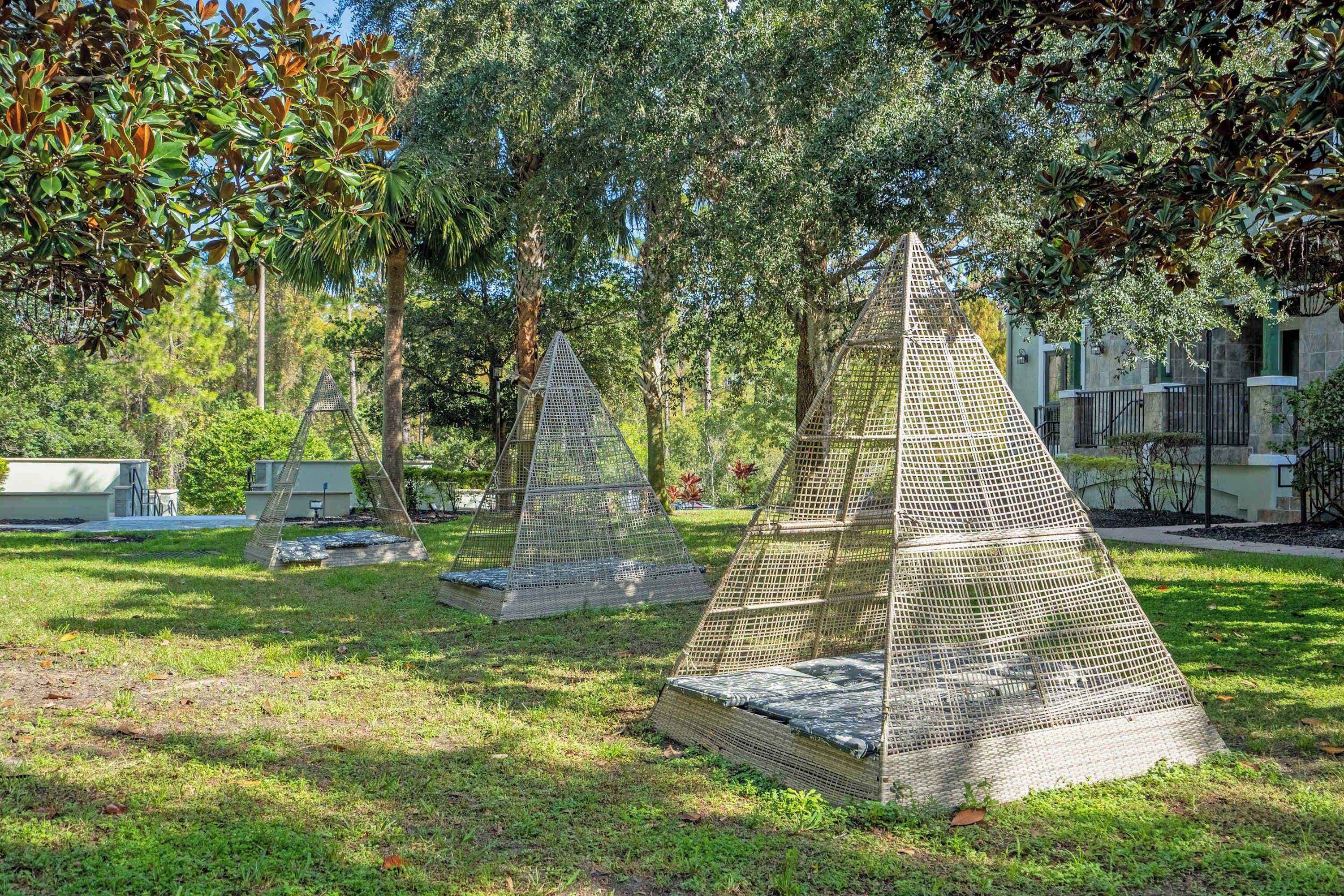 Outdoor seating areas with metal mesh structures and cushions, surrounded by trees and greenery.
