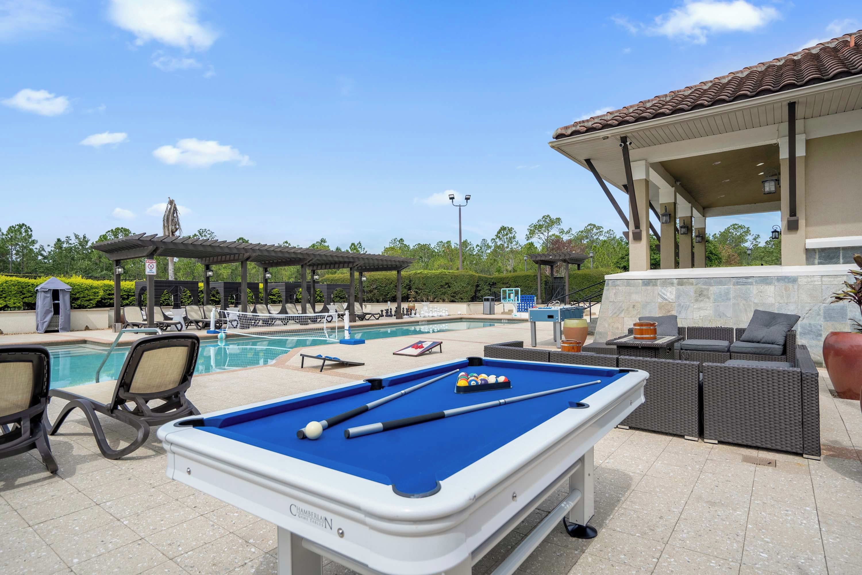 A pool area with a pool table, lounge chairs, and a covered seating area.