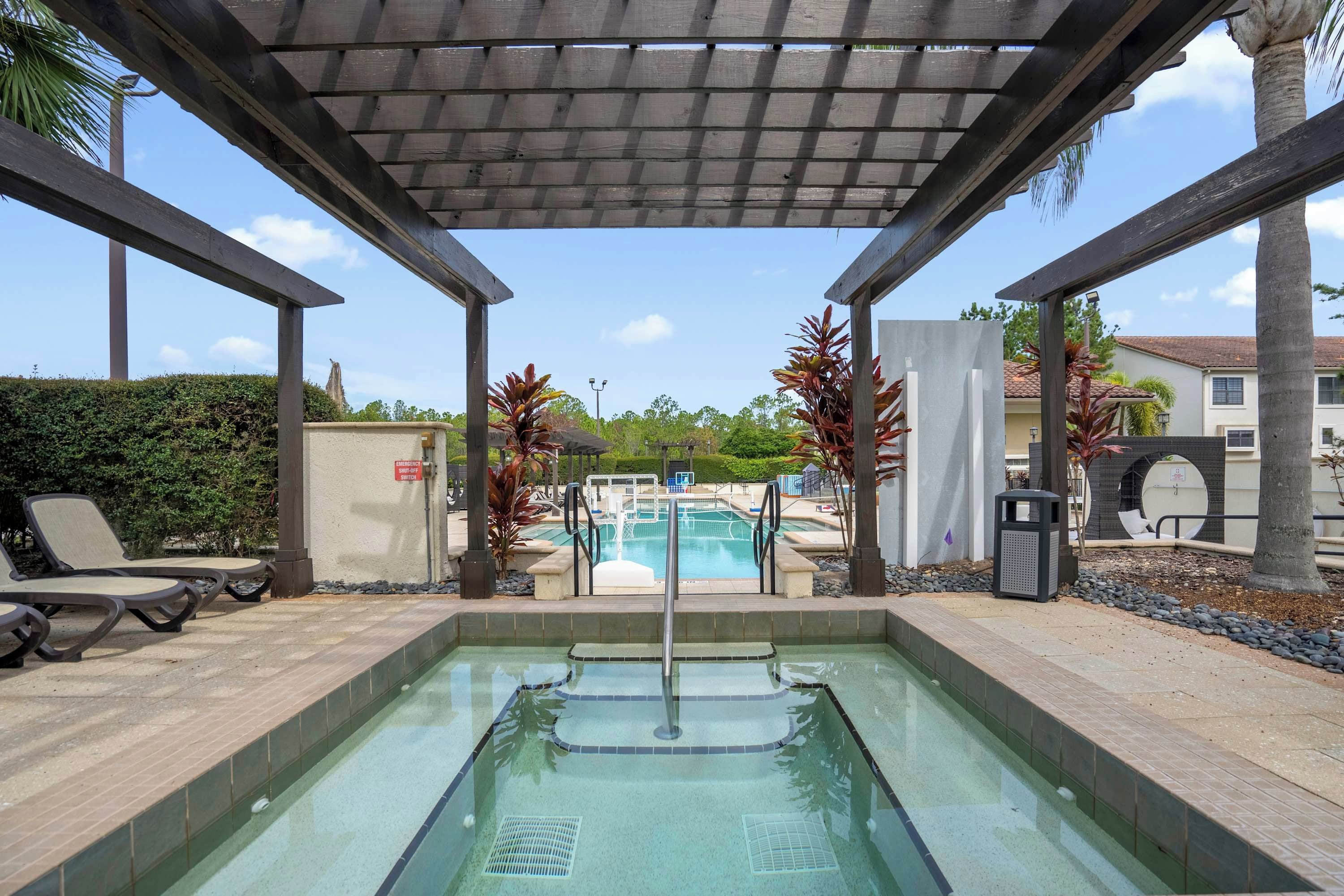 A pool area with a pergola overhead, lounge chairs, and a view of the pool.