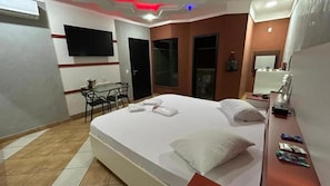 Une chambre d’hôtel avec un lit, un bureau, une chaise, un téléviseur fixé au mur et une fenêtre.