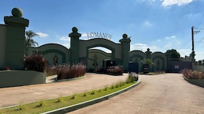 A gated entrance with the name 'ROMANUS' above it, surrounded by greenery and a clear sky. - Romanus Piracicaba (Piracicaba)
