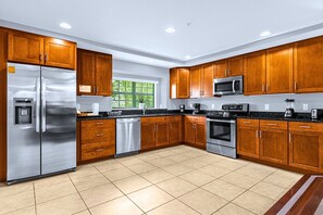 A modern kitchen with wooden cabinets, stainless steel appliances, and a tiled floor. - Family Townhome Near Disney w Pool & Giant Chess (Orlando)