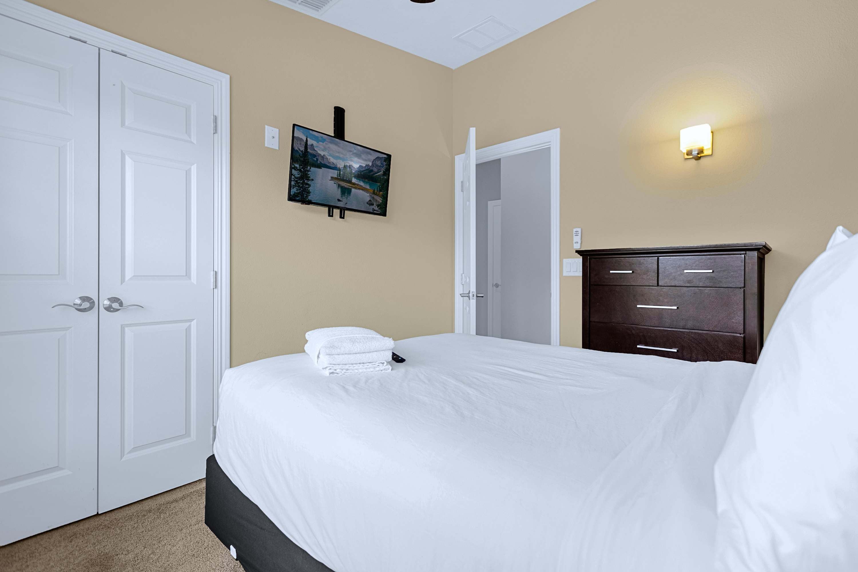 Quarto de hotel com cama, penteadeira, pintura e luminária na parede.
